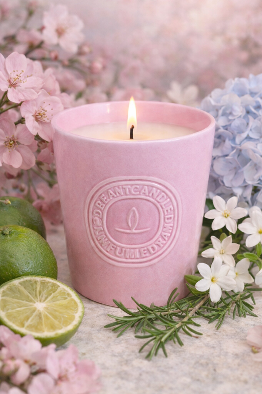 Lumine Cherry Blossom & White Jasmine soy wax candle lit in a styled ingredient scene with cherry blossom petals, white jasmine, rosemary sprigs and citrus peel.